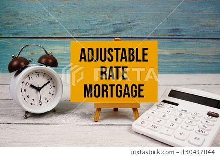 Adjustable-Rate Mortgage (ARM) text written on paper card with calculator and alarm clock on wooden background 130437044