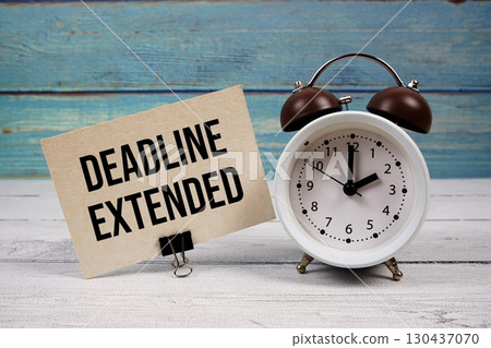 Deadline Extended text written on paper card with alarm clock on wooden background 130437070