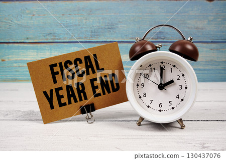 Fiscal Year End text written on paper card with alarm clock on wooden background 130437076
