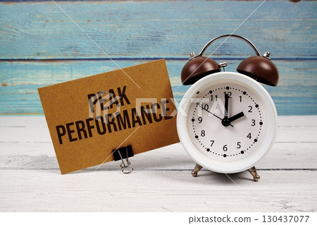 Peak Performance text written on paper card with alarm clock on wooden background 130437077