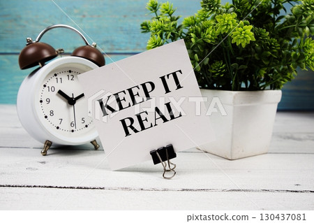 Keep It Real text written on paper card with alarm clock on wooden background 130437081