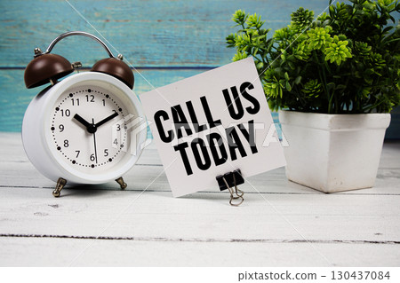 Call Us Today text written on paper card with alarm clock on wooden background 130437084