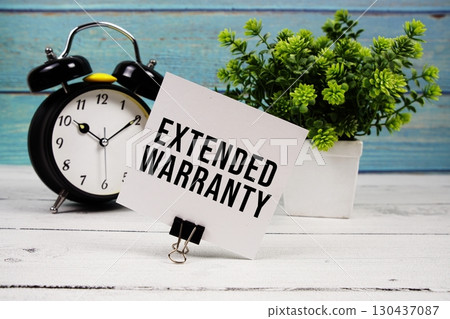 Extended Warranty text written on paper card with alarm clock on wooden background 130437087