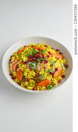 A colorful, appetizing dish of yellow rice mixed with vibrant vegetables and garnished with pomegranate seeds in a white bowl. Fresh herbs add an extra touch to the presentation 130437266
