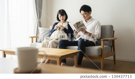 一位懷孕的妻子正在織毛衣，而她的丈夫則在旁邊看書 130437713