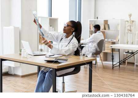 Young African woman doctor analyzing x-ray image at desk in contemporary clinic 130438764