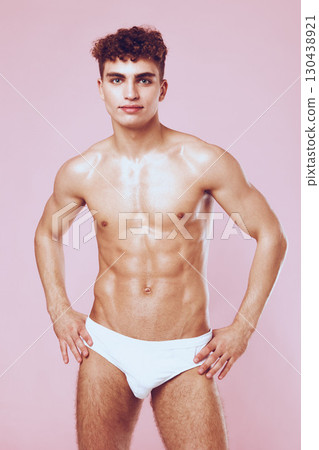Confident young man with athletic build posing in white swimwear against a pastel pink background. Fitness and body positivity concept. Confident young man with athletic build posing in white swimwear against a pastel pink background. Fitness and body positivity concept. 130438921