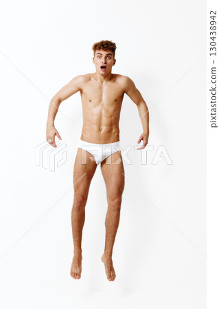 Surprised young man jumping with excitement, showcasing toned physique. White background emphasizing his expression and movement. Fitness and emotion concept. 130438942