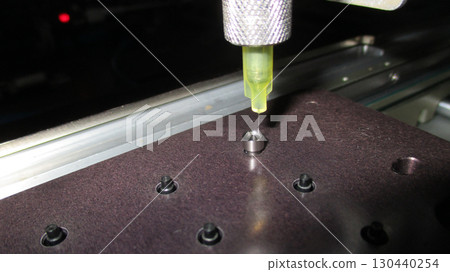 Automated machine with precision focus dispensing yellow glue from nozzle during an industrial manufacturing assembly process for high technology 130440254