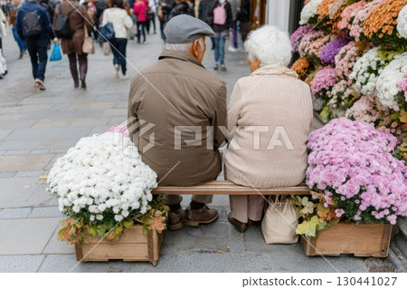 An elderly couple sits closely on a bench between colorful flowers, watching the busy street pass by. A peaceful moment captured amidst the hustle of a lively city scene An elderly couple sits closely on a bench between colorful flowers, watching the busy street pass by. A peaceful moment captured amidst the hustle of a lively city scene 130441027