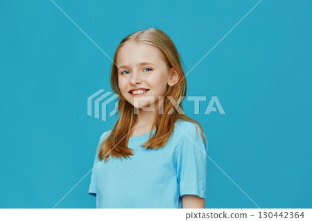 Happy girl with blonde hair smiling in a blue t shirt against a turquoise background, capturing joy and innocence, ideal for family and children related content 130442364