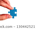A hand holding a puzzle piece. Female fingers with a blue jigsaw puzzle piece. 130442521