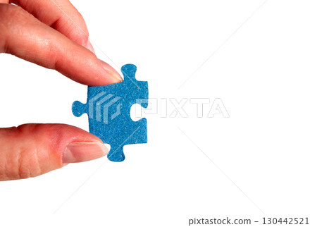A hand holding a puzzle piece. Female fingers with a blue jigsaw puzzle piece. 130442521