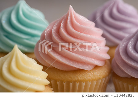 Cupcakes with pastel swirls in teal, pink, and yellow displayed close-up on neutral base 130442923