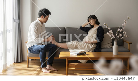 Husband massaging the feet of a pregnant woman lying on the sofa 130443647