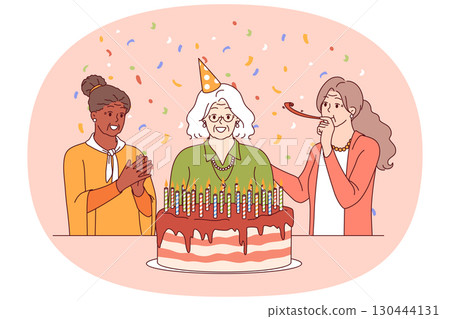 Birthday of elderly woman standing near large cake with candles and happy friends 130444131