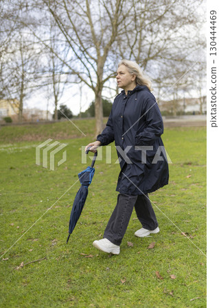 Woman walking in park with umbrella on cloudy day Woman walking in park with umbrella on cloudy day 130444469