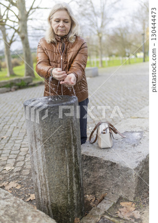 Senior woman washing hands in public park fountain on cold day 130444473