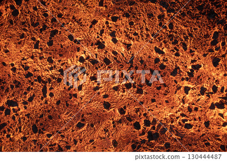 Close-up shot of glowing molten lava with bright orange cracks and a textured surface. 130444487