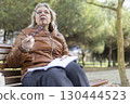 Senior woman thinking while reading a book on a bench in the park 130444523