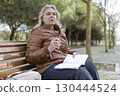 Senior woman thinking while reading a book on a bench in a park 130444524