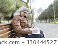Senior woman writing on notepad while sitting on bench in park 130444527