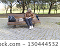 Senior woman writing in notebook while sitting on bench in park 130444532