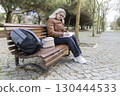 Senior woman writing notes in notebook while sitting on bench in park 130444533