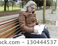 Senior woman writing in notebook while sitting on bench in park 130444537