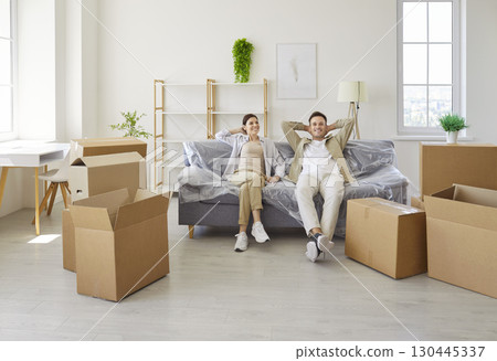 Happy couple relaxing on sofa amid moving boxes in bright new apartment interior Happy couple relaxing on sofa amid moving boxes in bright new apartment interior 130445337