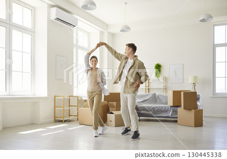 Couple twirling joyfully in bright new apartment with moving boxes and sunlight Couple twirling joyfully in bright new apartment with moving boxes and sunlight 130445338