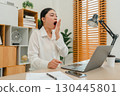 sleepy woman yawning while working with laptop computer at home office 130445801