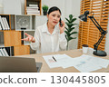 stressed woman talking with smartphone. working with document and laptop at home office 130445805