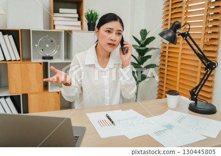 stressed woman talking with smartphone. working with document and laptop at home office 130445805