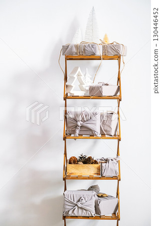 Furoshiki gift wrapping with Christmas decor on wooden shelf against white wall. 130446452