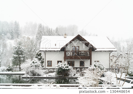 Modern home exterior and garden design. Cozy winter retreat in a snow-covered landscape. 130448654