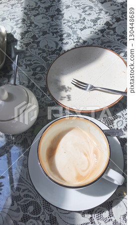 Coffee and empty plate on a lace tablecloth by the window in morning sunlight 130448689