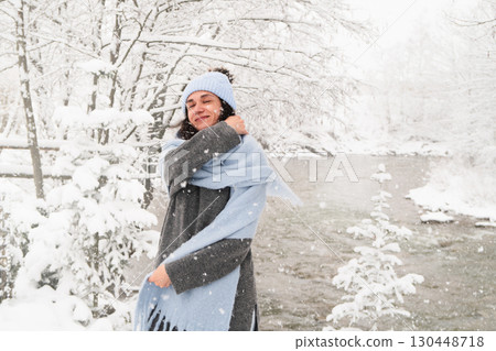 Joyful woman enjoying a snowy winter day by a tranquil river during the Christmas season 130448718
