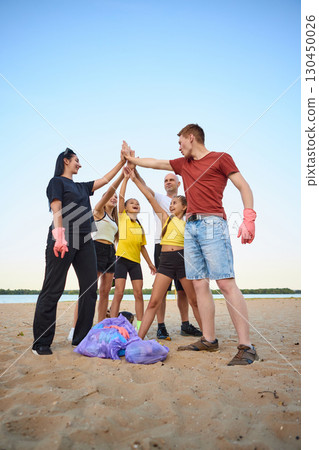 Happy family raising hands together on beach after cleaning trash 130450026