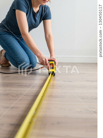 Woman measuring wooden floor with tape measure, home improvement project 130450117