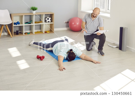 Exhausted overweight woman lying on floor while fitness trainer tries to motivate her 130450661