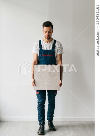 Focused man holding tile in minimalist space, interior design concept 130451163