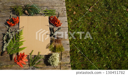 Cardboard model of an invitation or advertisement, on a wooden table surrounded by autumn berries and leaves. 130451782