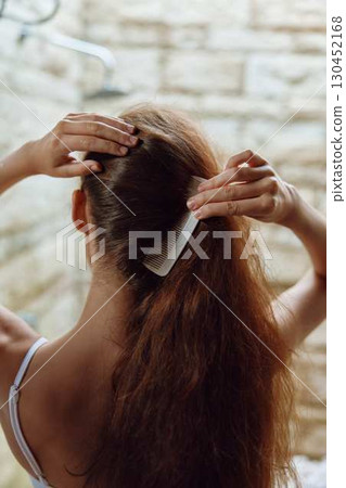 Woman combing long thick hair in a bright bathroom with natural light, showing careful grooming and hair care routine. Woman combing long thick hair in a bright bathroom with natural light, showing careful grooming and hair care routine. 130452168
