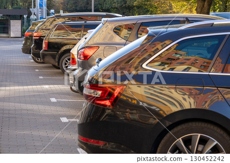 Several parked cars in a row show reflections of surrounding buildings under clear skies in a bustling urban setting 130452242