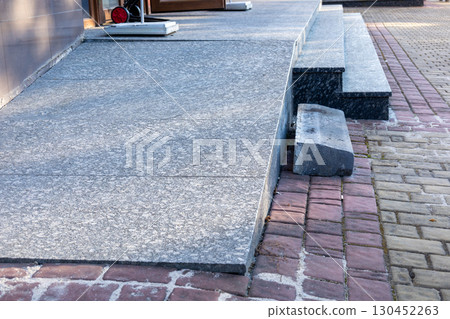 Smooth concrete ramp connects to textured bricks, enhancing accessibility at a modern building entrance during daylight hours 130452263