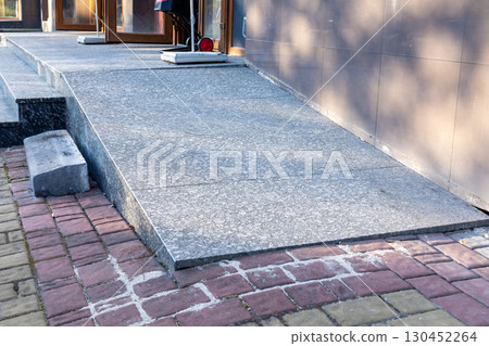 A smooth, accessible ramp connects a brick path to a concrete surface outside a public building, ensuring ease of access for all individuals 130452264