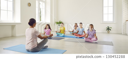 Group of children together with trainer sitting on mats,doing yoga and mediating Group of children together with trainer sitting on mats,doing yoga and mediating 130452288