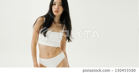 Young woman in white crop top posing indoors with minimal clean fashion style Young woman in white crop top posing indoors with minimal clean fashion style 130453580