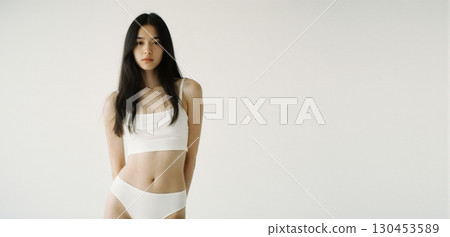 Young woman in white crop top posing indoors with minimal clean fashion style 130453589